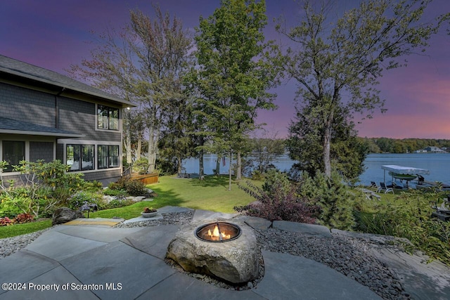 patio terrace at dusk featuring a fire pit, a water view, and a yard