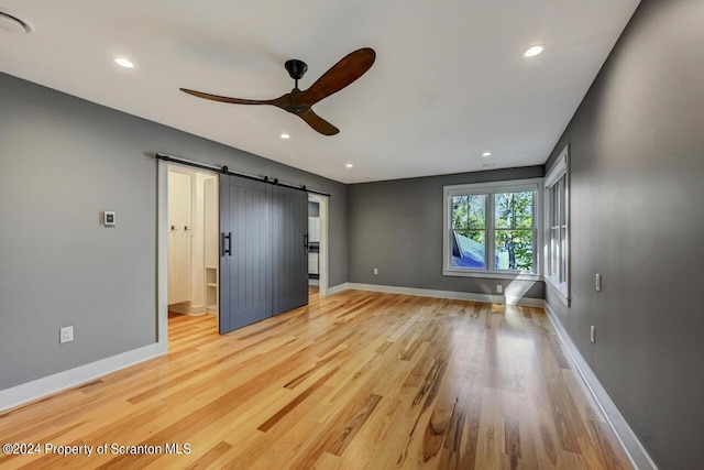 unfurnished bedroom featuring hardwood / wood-style flooring, ceiling fan, and a barn door