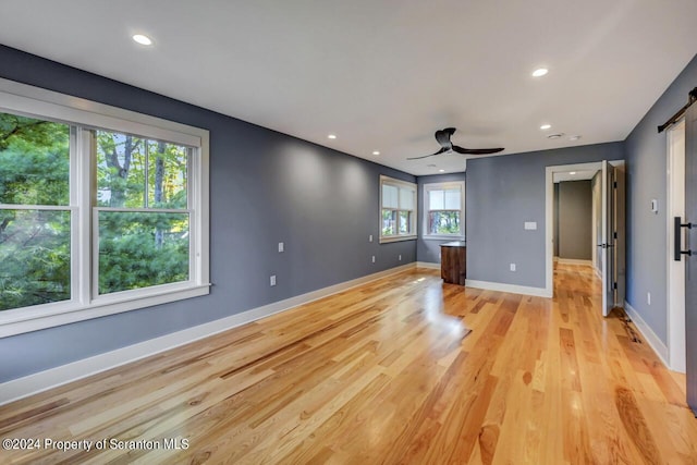 unfurnished living room featuring a barn door, ceiling fan, and light wood-type flooring