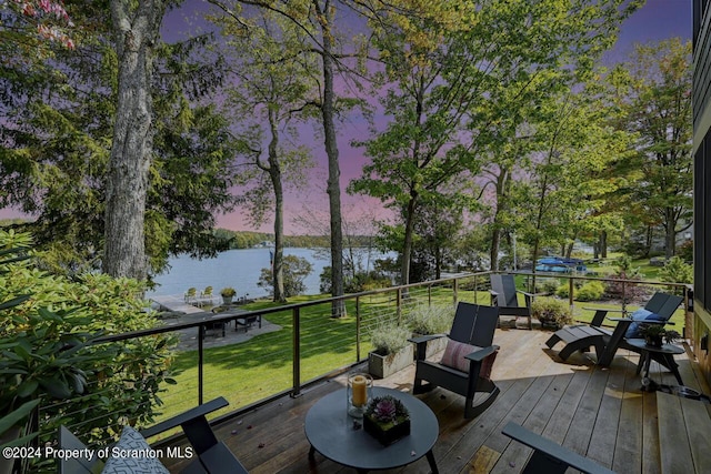 deck at dusk featuring a lawn and a water view