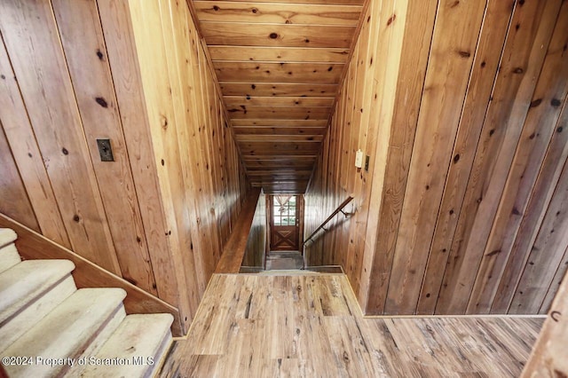 stairs featuring wood ceiling, wooden walls, wood-type flooring, and lofted ceiling