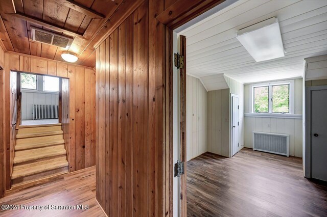 corridor with hardwood / wood-style floors, radiator heating unit, and wooden walls