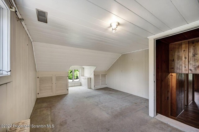 additional living space featuring light colored carpet, wooden walls, and vaulted ceiling