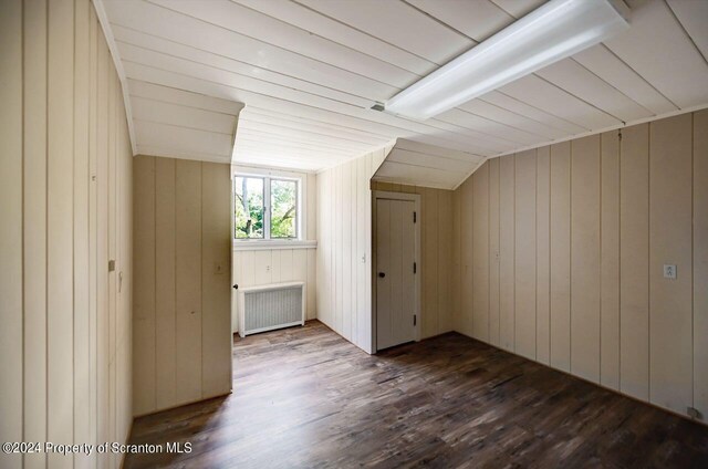 additional living space with wooden walls, radiator heating unit, lofted ceiling, and hardwood / wood-style flooring