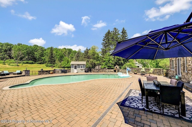 view of swimming pool with pool water feature, an outbuilding, and a patio