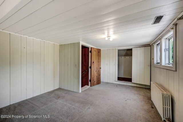 interior space with light colored carpet, radiator, and wood walls