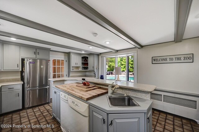 kitchen featuring stainless steel refrigerator, dishwasher, sink, gray cabinets, and a kitchen island with sink