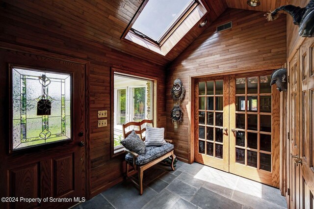 entrance foyer featuring vaulted ceiling with skylight, wood walls, wood ceiling, and french doors