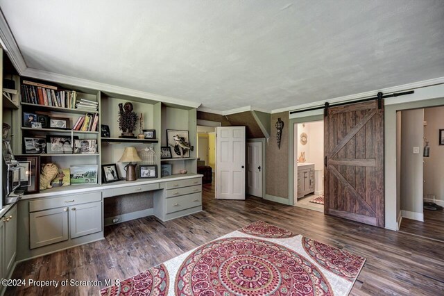 office space with a barn door, built in desk, dark hardwood / wood-style floors, and ornamental molding