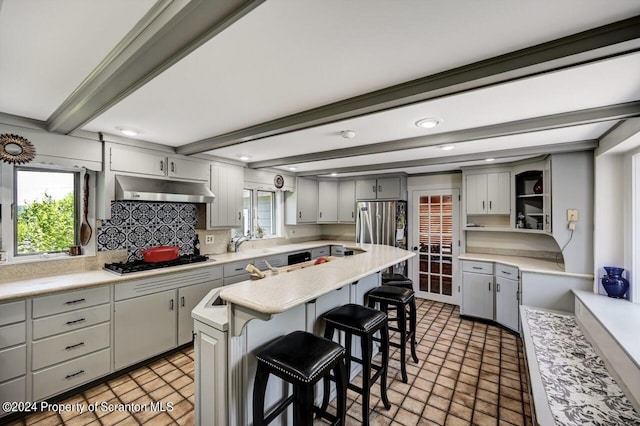 kitchen with beam ceiling, a kitchen breakfast bar, gray cabinets, a kitchen island, and appliances with stainless steel finishes