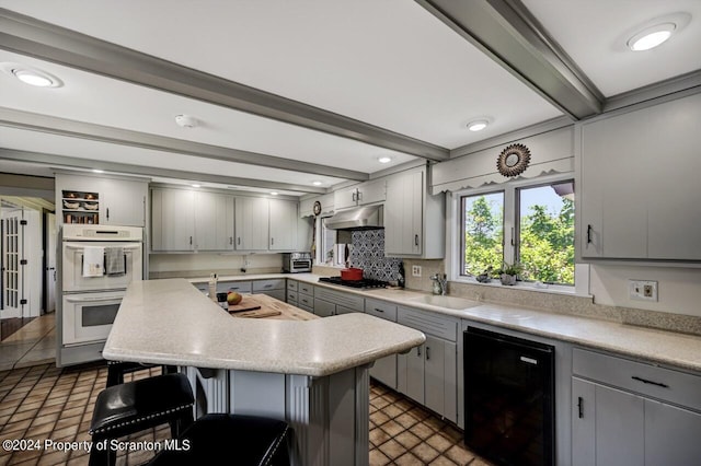 kitchen with refrigerator, gray cabinetry, a breakfast bar, double oven, and beamed ceiling