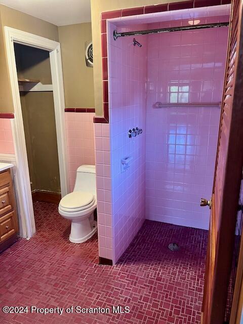 bathroom featuring tiled shower, vanity, tile walls, and toilet