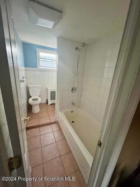 bathroom with tile walls, tile patterned flooring, radiator heating unit, toilet, and tiled shower / bath