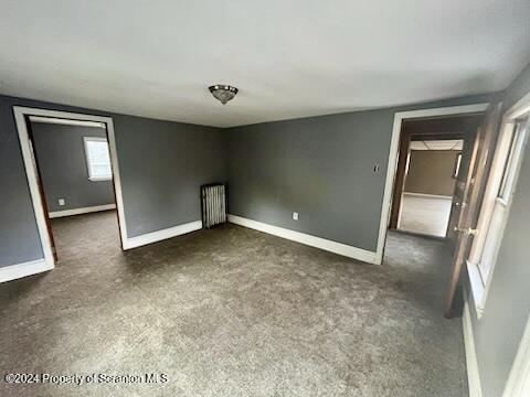 unfurnished room featuring radiator heating unit and dark carpet