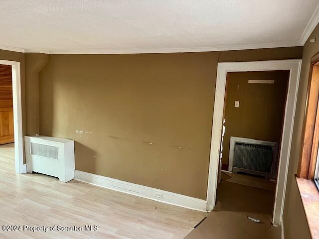 empty room featuring a textured ceiling, light hardwood / wood-style floors, radiator, and ornamental molding