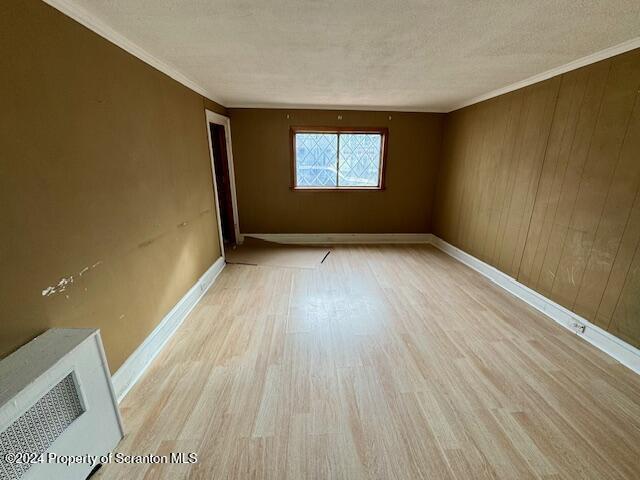 unfurnished room featuring wood walls, crown molding, a textured ceiling, and light hardwood / wood-style flooring