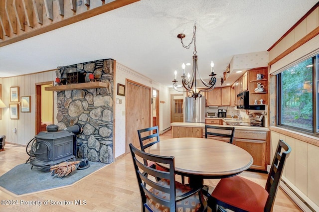 dining space featuring light wood-type flooring, a textured ceiling, a baseboard radiator, a notable chandelier, and a wood stove