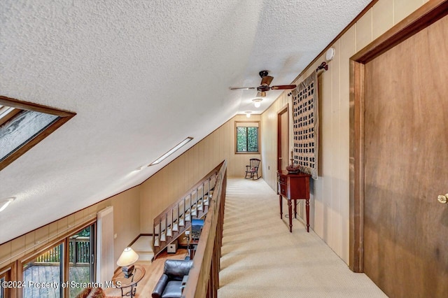 hall featuring wood walls, light colored carpet, and vaulted ceiling