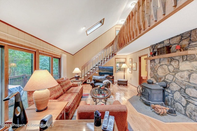 living room featuring ornamental molding, high vaulted ceiling, light hardwood / wood-style floors, a wood stove, and wood walls