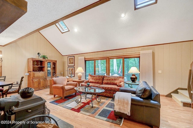 living room featuring a textured ceiling, light hardwood / wood-style flooring, wooden walls, and vaulted ceiling with skylight