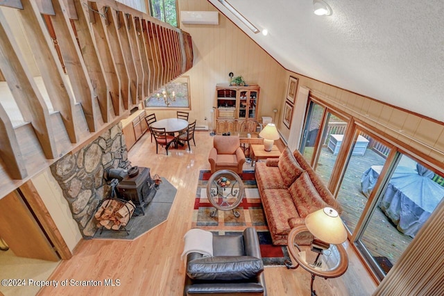 living room featuring a wood stove, wood walls, a textured ceiling, vaulted ceiling, and hardwood / wood-style flooring