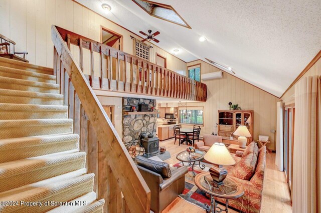 living room with a wood stove, high vaulted ceiling, wooden walls, ceiling fan, and a textured ceiling