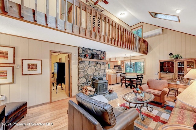 living room with lofted ceiling with skylight, an AC wall unit, an inviting chandelier, light hardwood / wood-style flooring, and a wood stove