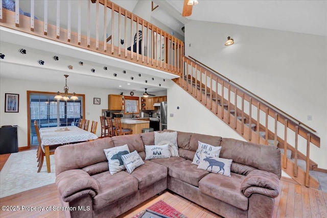 living area featuring ceiling fan with notable chandelier, light wood-type flooring, a towering ceiling, and stairs