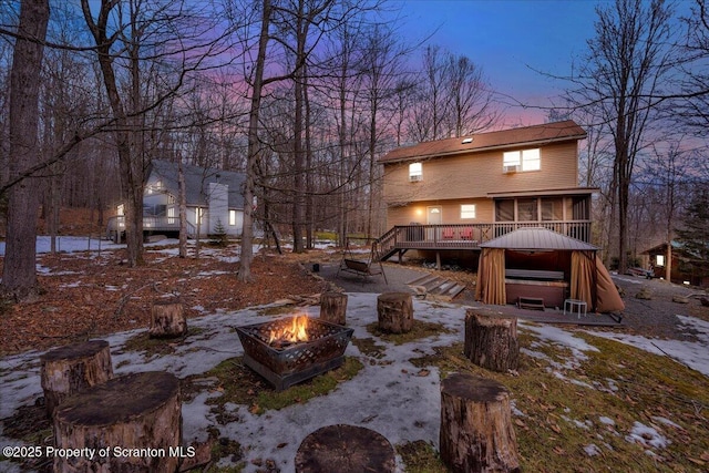 back of property at dusk featuring a sunroom, an outdoor fire pit, and a wooden deck