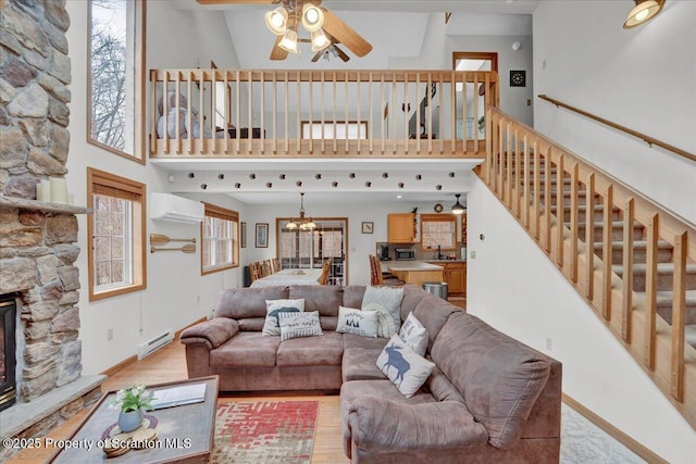 living room with a wall unit AC, a towering ceiling, stairway, a stone fireplace, and light wood-style floors