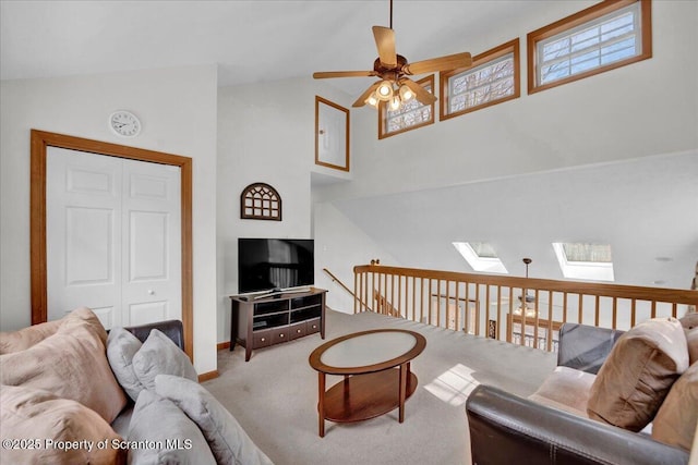 living area featuring a ceiling fan, a skylight, high vaulted ceiling, and carpet