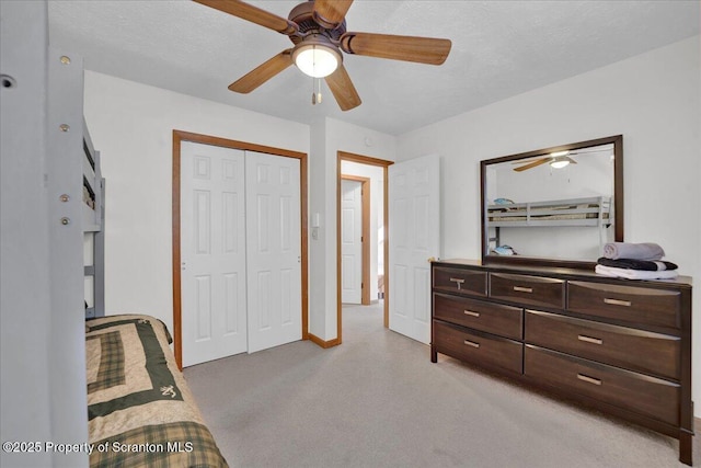 bedroom with ceiling fan, a textured ceiling, light colored carpet, baseboards, and a closet