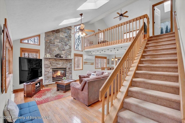 living area with ceiling fan with notable chandelier, a stone fireplace, light wood finished floors, and stairway