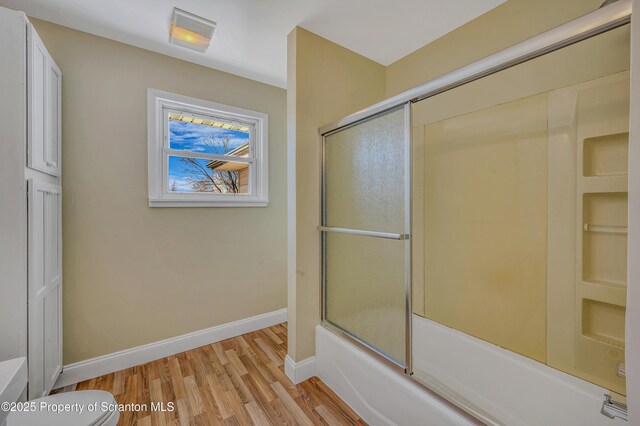 bathroom with enclosed tub / shower combo, baseboards, toilet, and wood finished floors