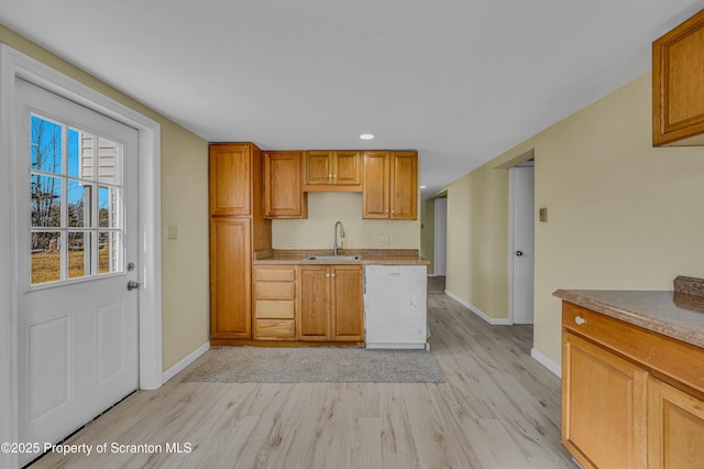 kitchen with light wood finished floors, baseboards, white dishwasher, brown cabinetry, and a sink