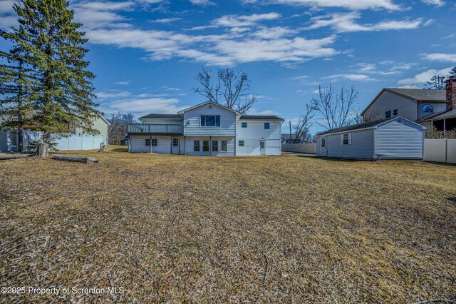 back of house featuring a lawn, an outdoor structure, and fence