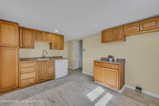 kitchen with a sink, baseboards, light wood-style floors, and dishwasher