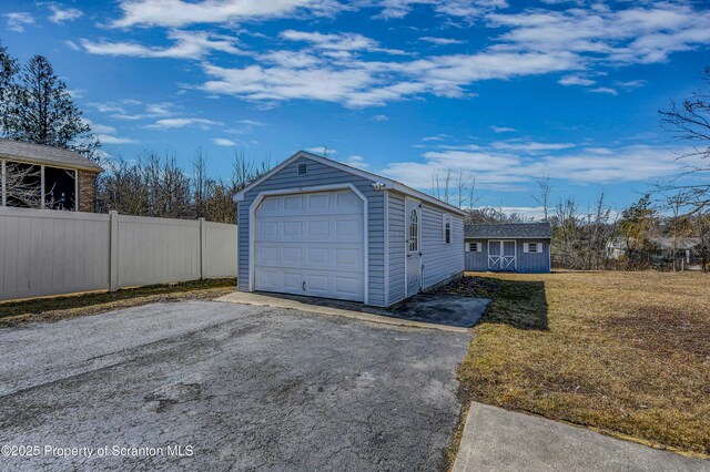 detached garage featuring aphalt driveway and fence