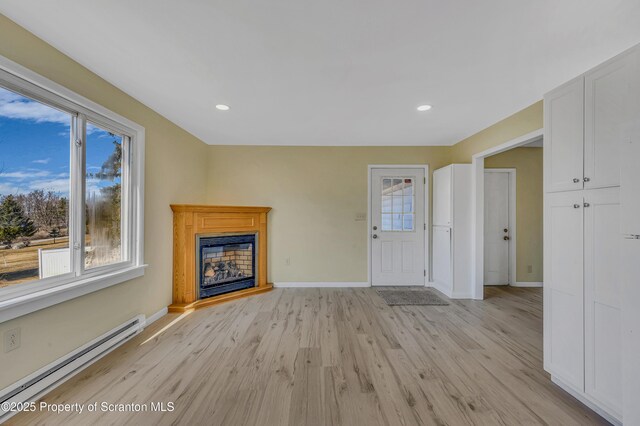 unfurnished living room featuring a baseboard radiator, baseboards, light wood-style flooring, and a fireplace