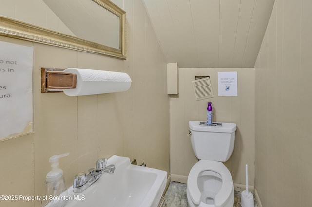 bathroom with toilet, vaulted ceiling, and wooden walls