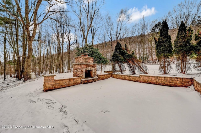 snow covered patio with an outdoor stone fireplace