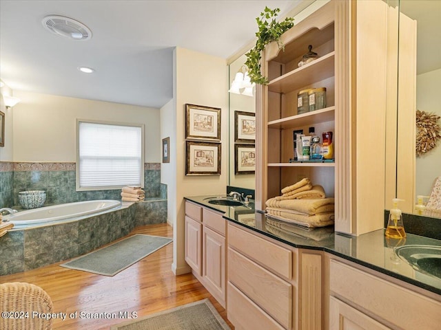 bathroom with hardwood / wood-style floors, vanity, and tiled tub