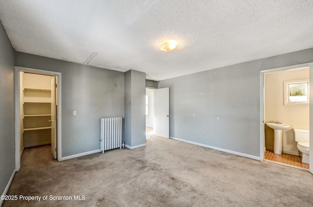 unfurnished bedroom featuring a textured ceiling, radiator heating unit, a sink, and a spacious closet