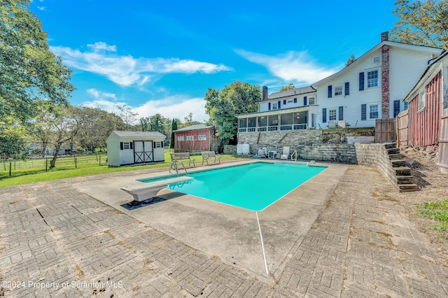 view of swimming pool with a diving board, a shed, and a patio area