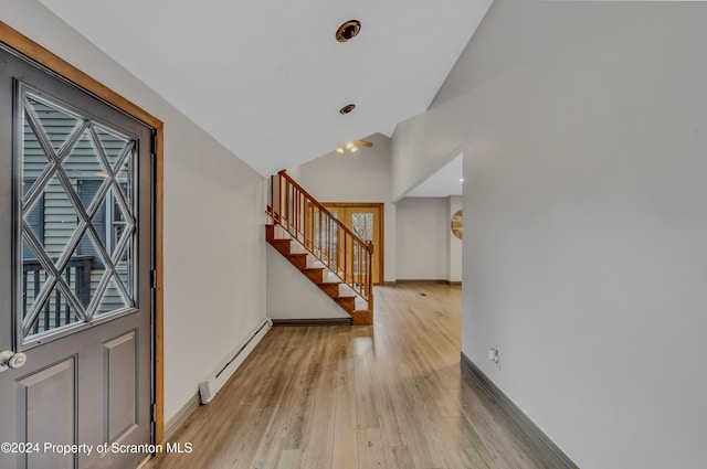 entrance foyer with a baseboard radiator, lofted ceiling, and light wood-type flooring