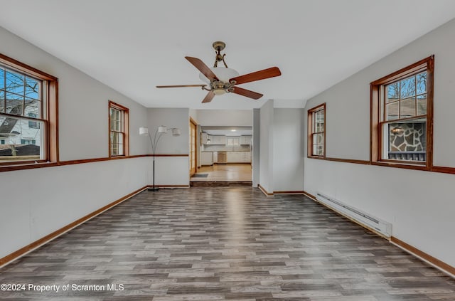 empty room featuring baseboard heating, ceiling fan, light hardwood / wood-style flooring, and a healthy amount of sunlight