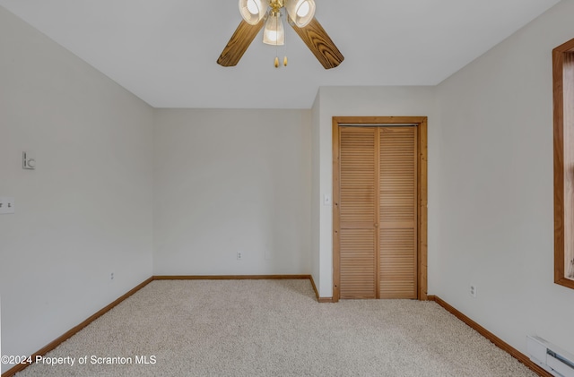 unfurnished bedroom featuring ceiling fan, a closet, light colored carpet, and a baseboard heating unit