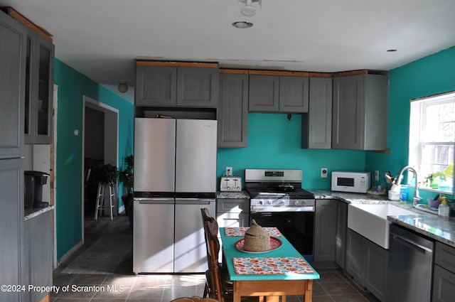 kitchen with light stone countertops, stainless steel appliances, gray cabinets, and sink