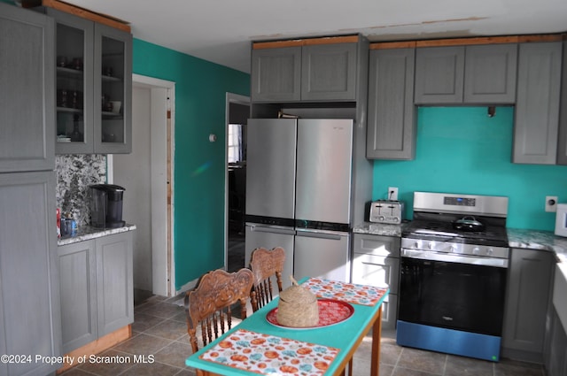 kitchen featuring decorative backsplash, stainless steel appliances, gray cabinets, and light stone counters