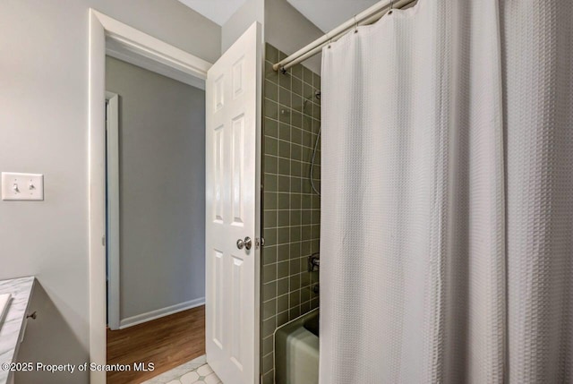 bathroom with baseboards, shower / bathtub combination with curtain, and wood finished floors